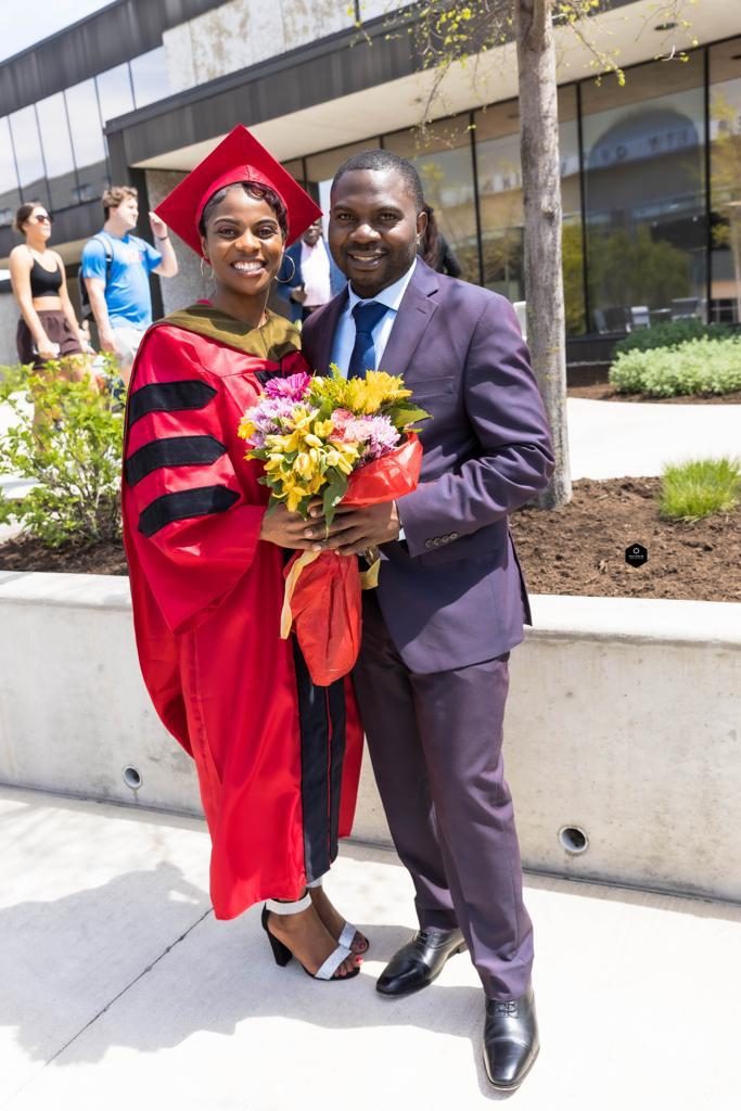A graduate in a red doctoral gown holding flowers