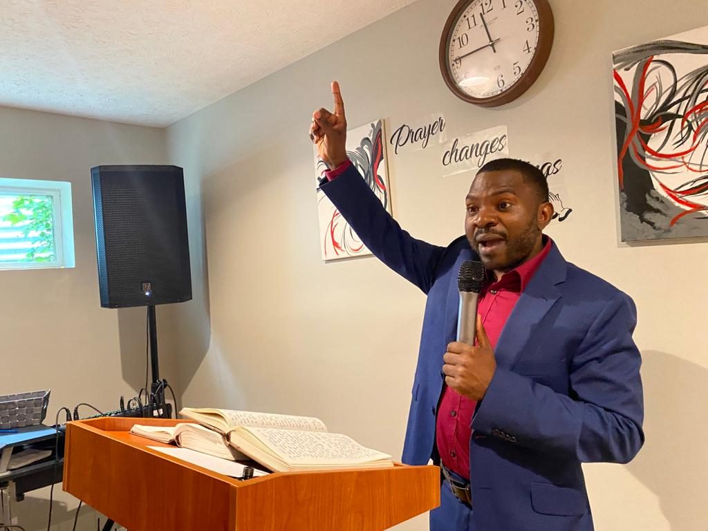 Pastor Elvis Eghombi preaching with an open Bible on the pulpit